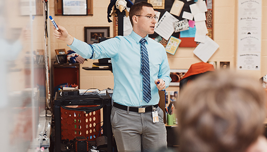 A young man pointing at a whiteboard and explaining something to a group