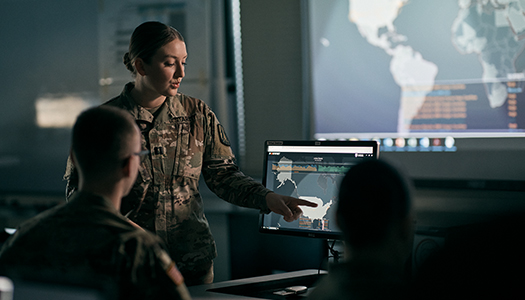 A Navy service member working on a computer in an operatons room