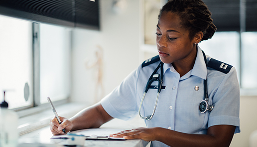 An Air Force physician is seated at a table writing on a clipboard