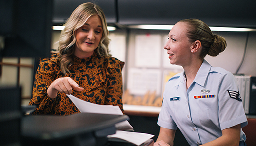 A Military service member chatting with another woman holding up a sheet of paper