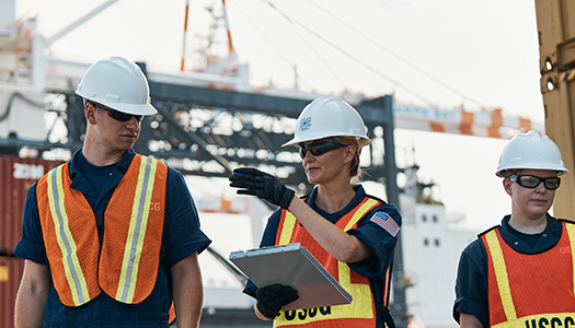 Three US coast Guard members standing at a port while holding a checklist board